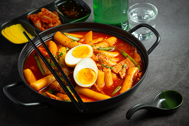 Cheesy Tokbokki korean traditional food on black board background. Lunch dish.